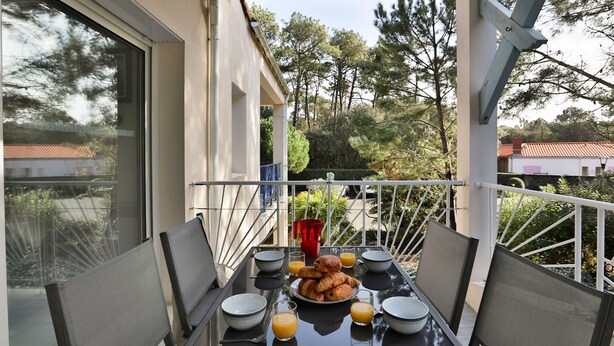 Un balcone con un tavolo apparecchiato per la colazione, con croissant e succo d'arancia, e sedie dallo schienale a rete.