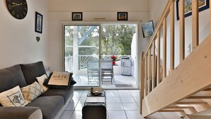 Un interno moderno con un divano, una scala in legno, un balcone con mobili da esterno e una grande finestra.