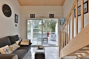 Ein modernes Interieur mit einer Couch, einer Holztreppe, einem Balkon mit Gartenmöbeln und einem großen Fenster.