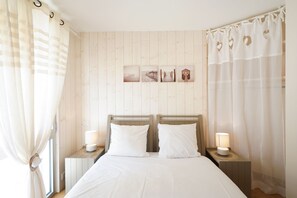 Ein Schlafzimmer mit einer holzverkleideten Wand, einem Bett mit weißen Leinen, zwei Nachttischlampen und einem Fenster mit Vorhängen.