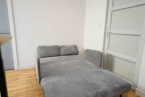 Ein kleines Zimmer mit einem Einzelbett, Holzboden, einer grauen Matratze und einer weißen Tür.
