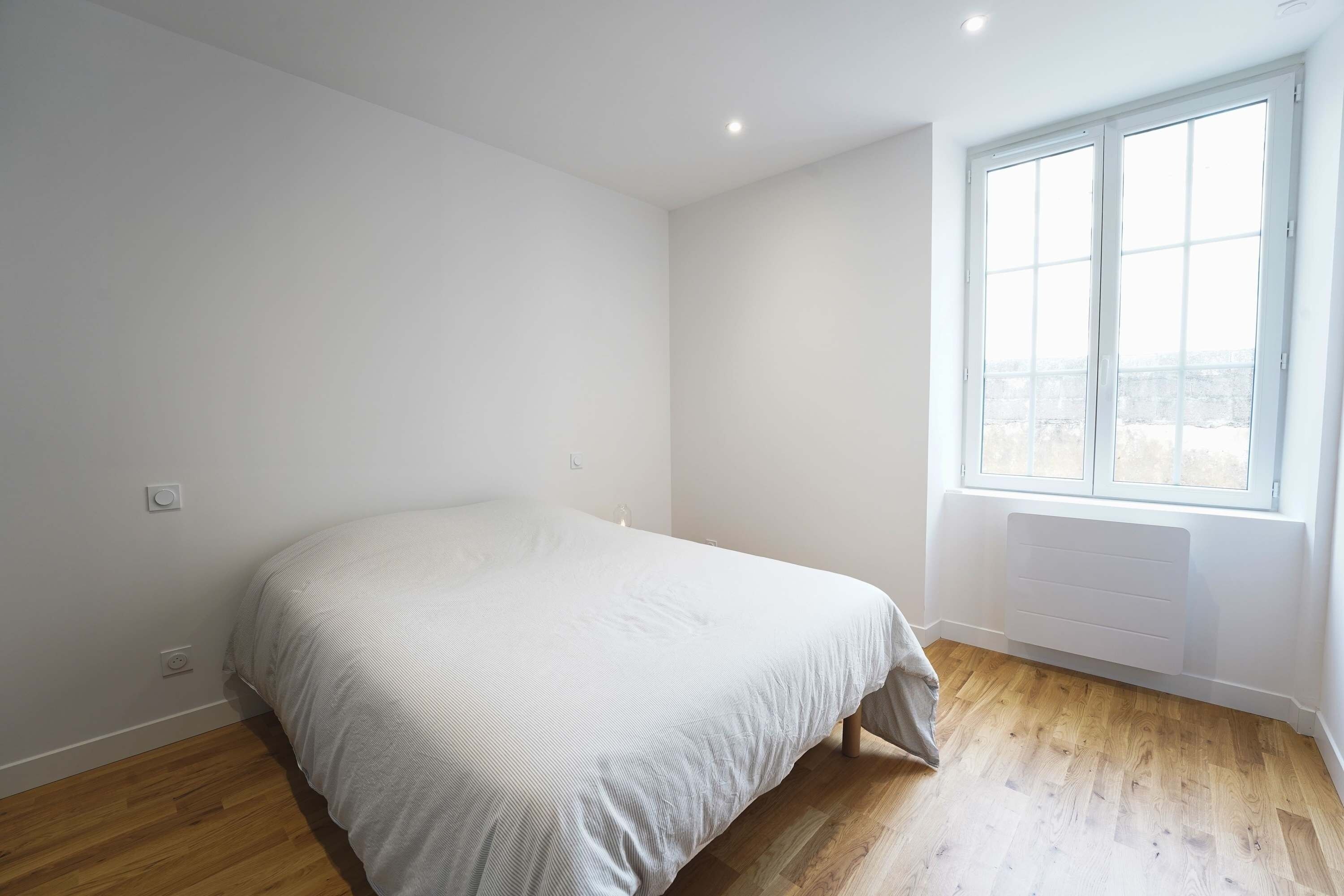 A bedroom with a bed, wooden flooring, a window, and a radiator.