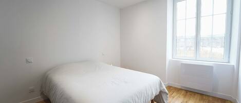 A bedroom with a bed, wooden flooring, a window, and a radiator.