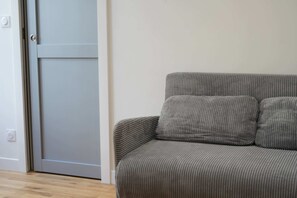 Ein graues Sofa mit einem Kissen, eine geschlossene Tür und ein Lichtschalter an der Wand.
