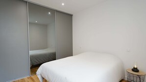 A bedroom with a bed, a bedside table with a lamp, and a sliding closet door. - Les Halles Sablaises (Les Sables d'Olonne)