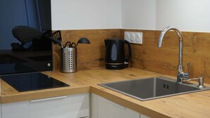 A modern kitchen with a built-in induction cooktop, a stainless steel sink, and a kettle. - Les Halles Sablaises (Les Sables d'Olonne)