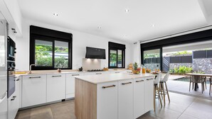 Une cuisine moderne avec des meubles blancs, un îlot central en bois et un coin repas doté d’un espace pour s’asseoir à l’extérieur.