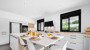 Une cuisine moderne avec des meubles blancs, un îlot central où l’on peut prendre le petit-déjeuner, et une grande fenêtre offrant une belle vue.