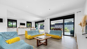 Un salon moderne avec une table basse en verre, des canapés jaunes et une cuisine en arrière-plan.