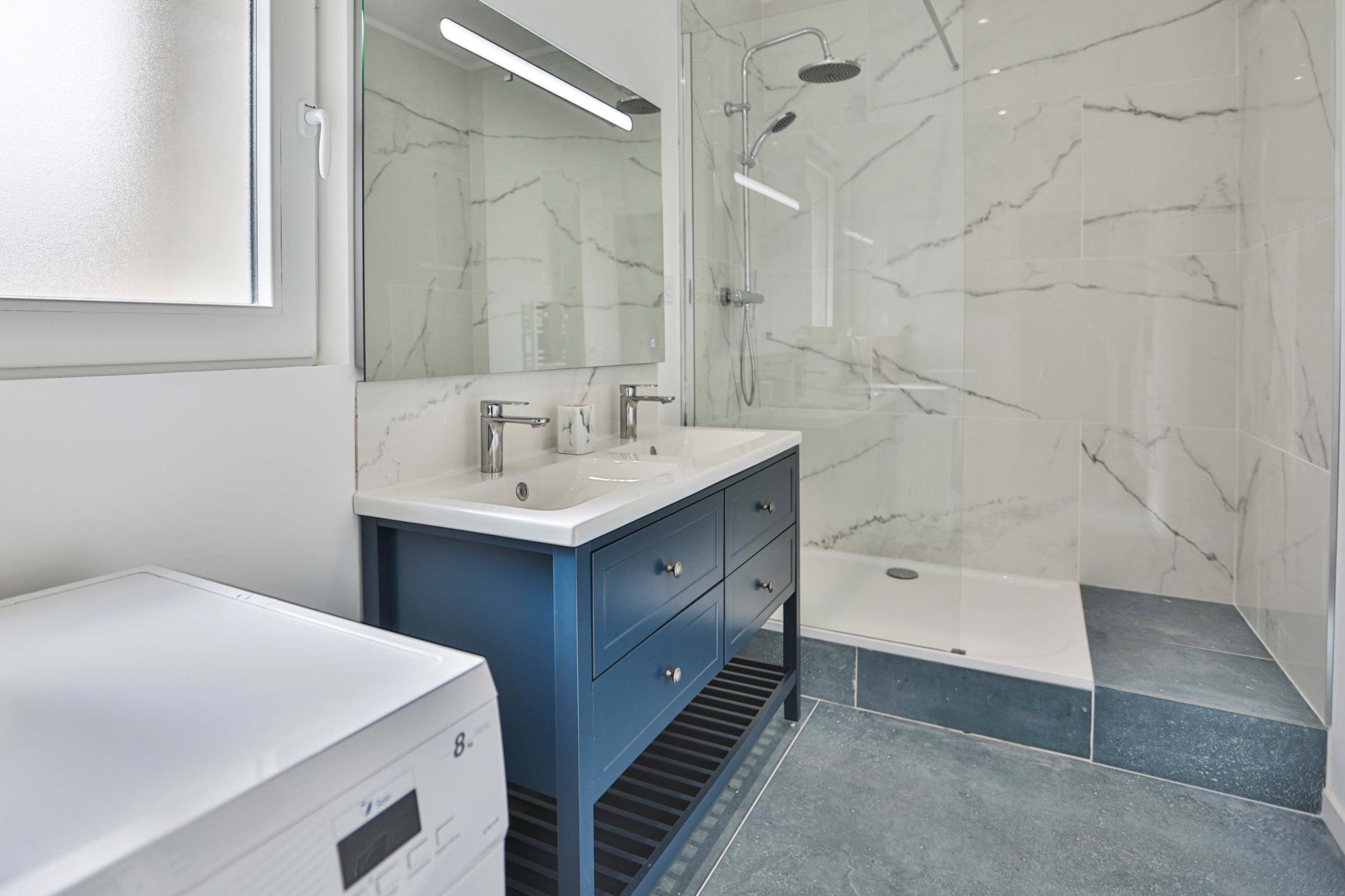 A modern bathroom with a white sink, blue cabinet, and a glass-enclosed shower area.