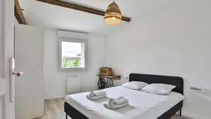Ett sovrum med en säng, ett fönster, ett element, en hängande lampa och en dörr.