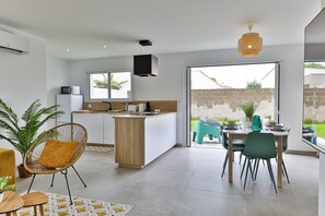 A modern kitchen with a central island, a dining area with chairs, and a large sliding glass door to the outside. - La Marinière des Sables (Les Sables d'Olonne)