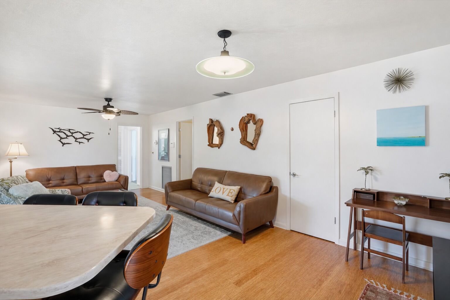 A living room with a brown leather sofa, a dining table, and a wooden desk with chairs.