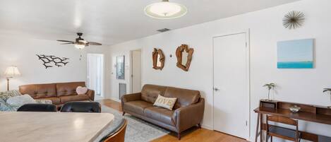 A living room with a brown leather sofa, a dining table, and a wooden desk with chairs.
