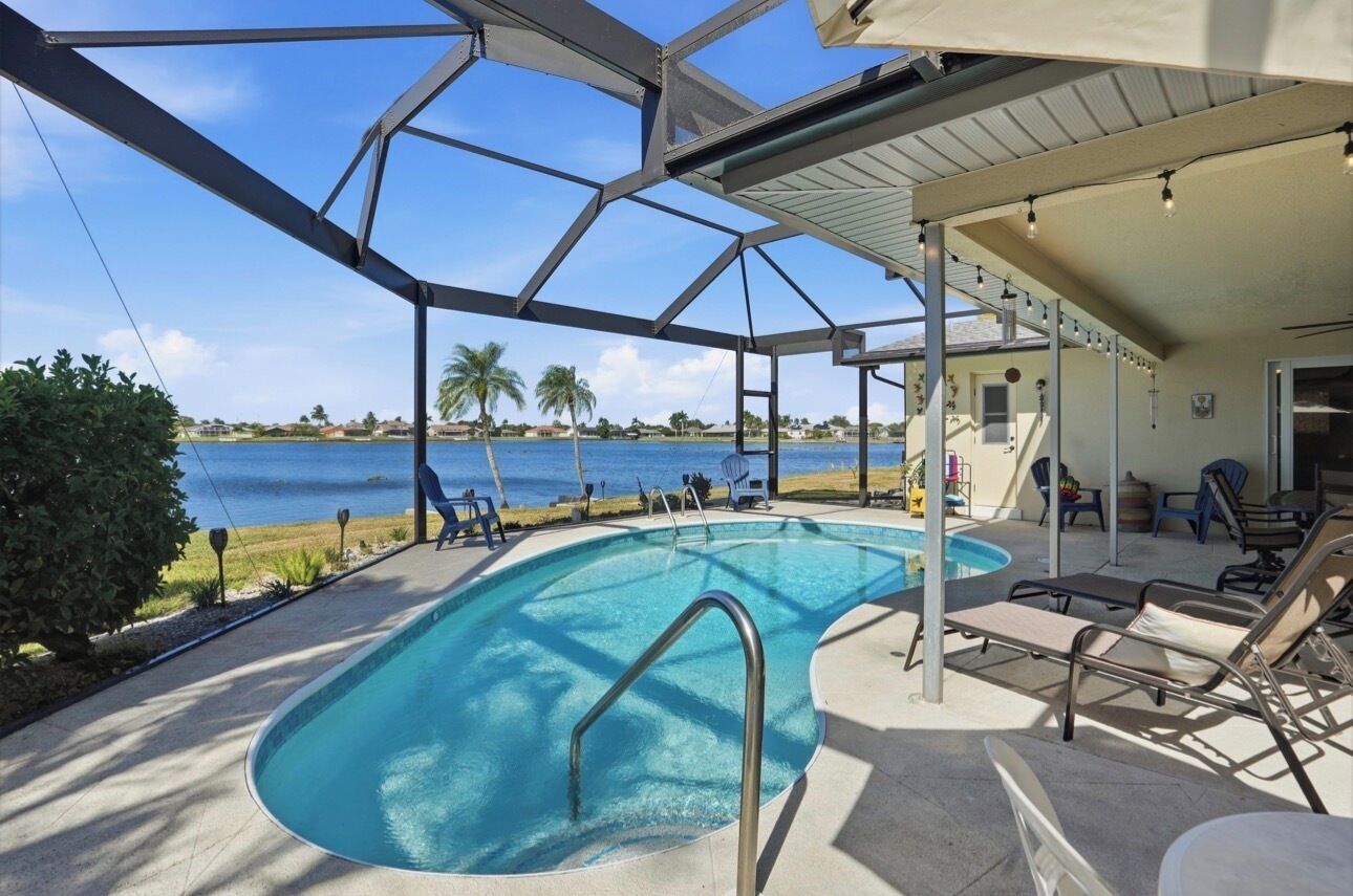 Una piscina con vista despejada al océano, un patio cubierto con sillas y vista a la playa.