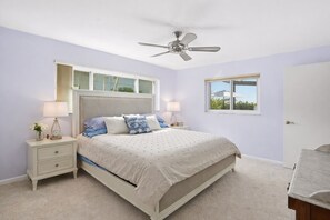 A bedroom with a bed, nightstands, a ceiling fan, a window, and a door. - Waterfront Villa with Heated Pool & Stunning Sunset Views (Cape Coral)