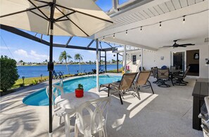 A poolside area with a view of the water, outdoor seating, and a ceiling fan. - Waterfront Villa with Heated Pool & Stunning Sunset Views (Cape Coral)