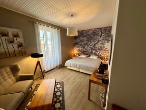 Ein Schlafzimmer mit Bett, Sessel, Tisch, Lampe und Wand mit Baumdesign.