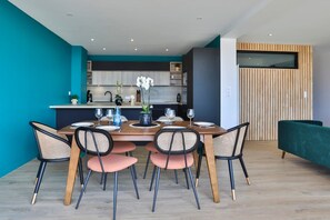 A modern dining area with a wooden table, six chairs, and a kitchen in the background. - Miramar - avec vue époustouflante sur la baie des Sables-d'Olonne (Les Sables d'Olonne)