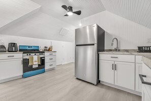 Una cocina moderna con armarios blancos, un refrigerador de acero inoxidable, un horno azul y un ventilador de techo.