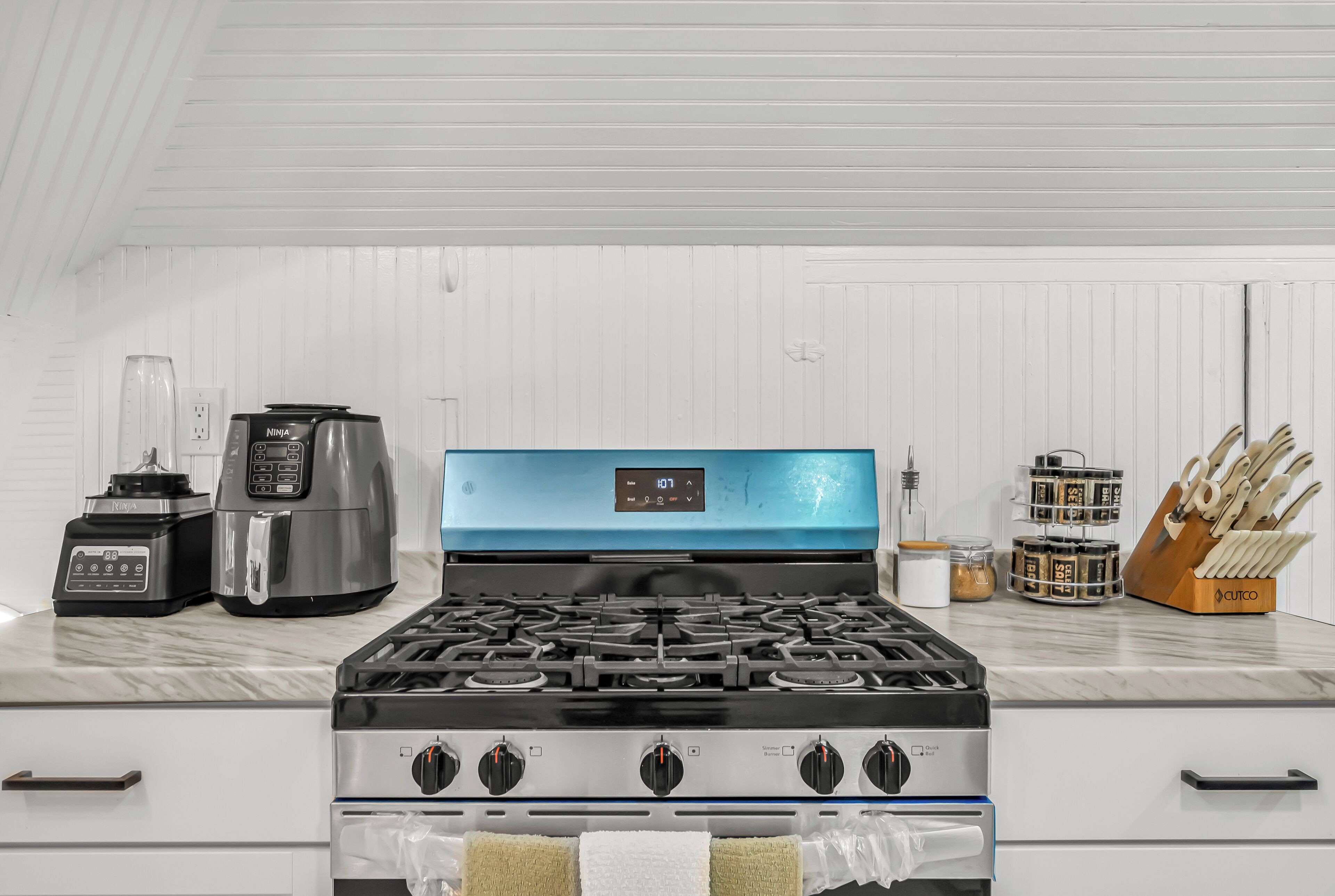 Une cuisine équipée d’une cuisinière à gaz, d’une machine à café, d’un mixeur et d’un bloc à couteaux.