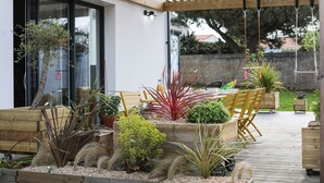 Una terraza de madera con macetas, un pérgola y muebles de exterior.