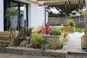 A wooden deck with planters, a pergola, and outdoor furniture. - La Bulle - Maison classée 4* (Brem-sur-Mer)