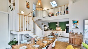 Un comedor amplio con una mesa de madera dispuesta para una comida, una escalera que conecta dos pisos, y un área de cocina visible al fondo.