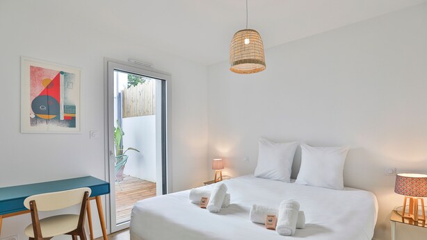 Un dormitorio con cama, escritorio, silla, lámpara colgante y puerta que da a un espacio exterior.