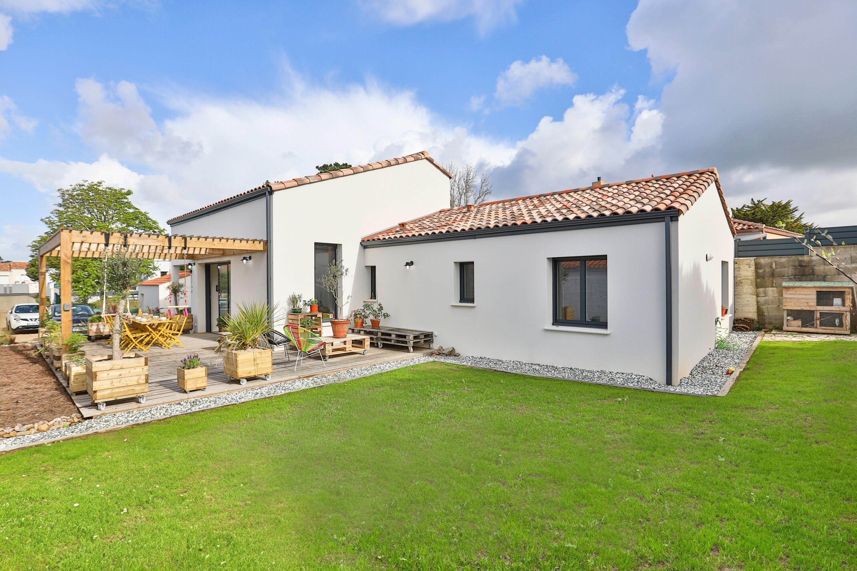 A modern two-story house with a tiled roof, a patio with outdoor furniture, and a well-maintained lawn.
