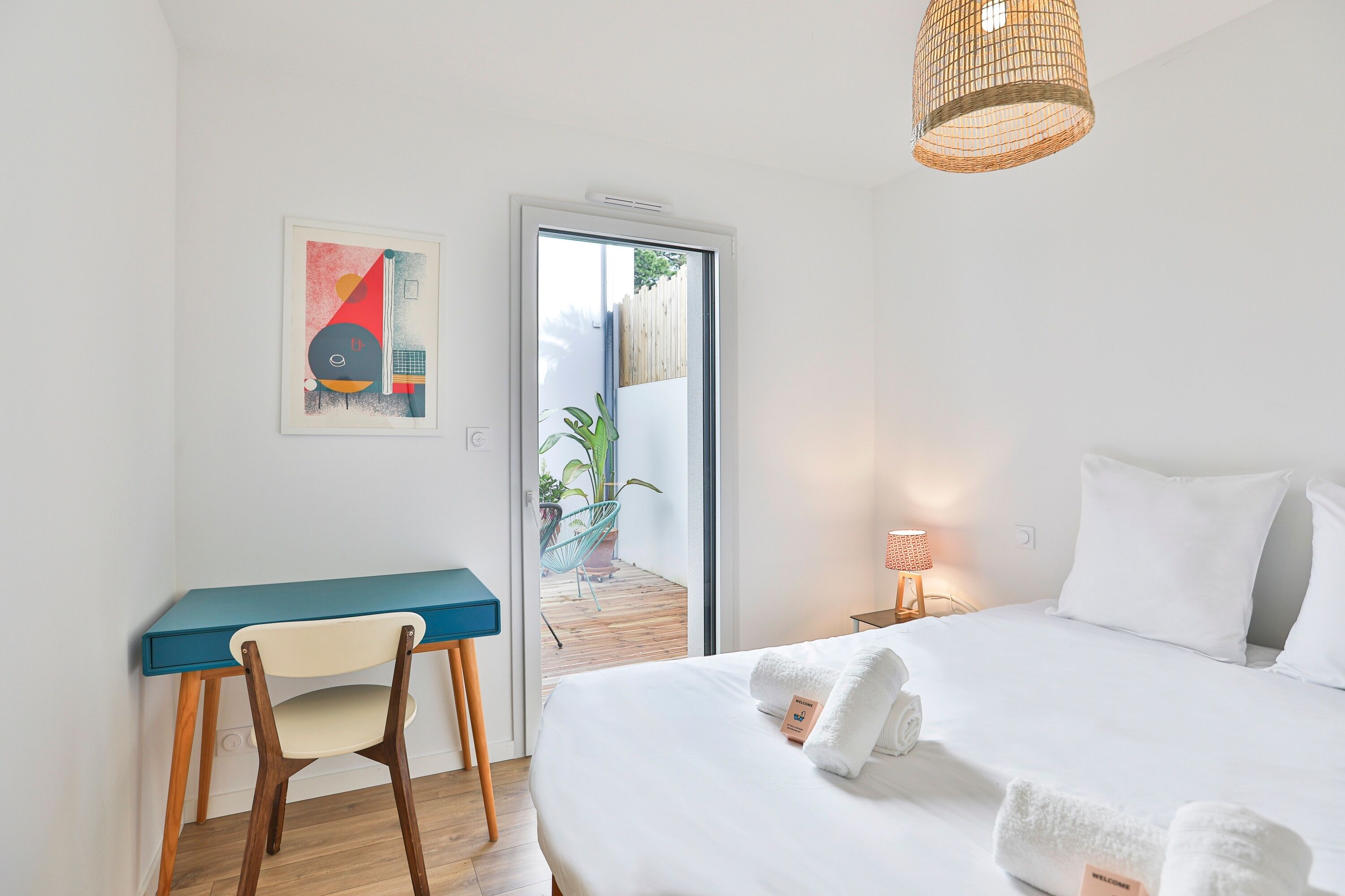 A bedroom with a bed, a desk, a chair, a door leading to a balcony, and a wall-mounted artwork.