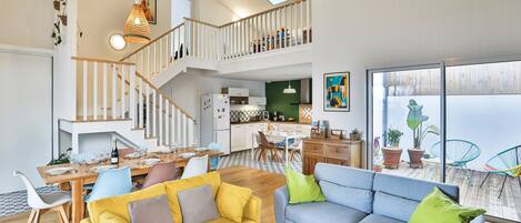 A spacious living area with a staircase, dining table, sofas, and a kitchen.