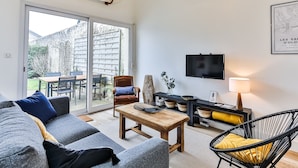 A modern living room with a surfboard, a TV, and a dining area with a table and chairs. - Maison des Surfeurs - Two Bedroom House, Sleeps 5 (Les Sables d'Olonne)