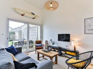 Una sala de estar moderna con una tabla de surf, un televisor y un comedor con una mesa y sillas.