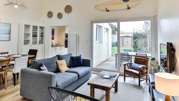 A modern living room with a grey sofa, wooden coffee table, and a dining area with a white table and chairs. - Maison des Surfeurs - Two Bedroom House, Sleeps 5 (Les Sables d'Olonne)