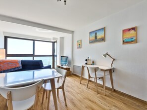 Ein modernes Zimmer mit großem Fenster, Schreibtisch, Stuhl, Lampe und Kunstwerk an der Wand.