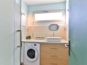 Une petite salle de bain équipée d’un lave-linge, d’un lavabo et d’un miroir.