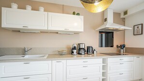 Eine moderne Küche mit weißen Schränken, einer eingebauten Spüle, einer Kaffeemaschine und einer Pendelleuchte.