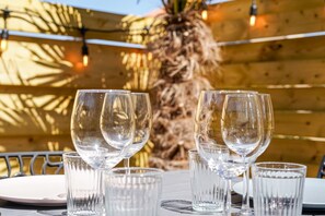 A table with clear glasses and plates, set against a wooden fence and palm tree, suggesting an outdoor dining area. - L'Escale Sablaise - Two Bedroom House, Sleeps 4 (Les Sables d'Olonne)