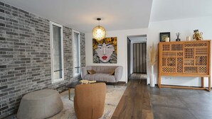 A modern living room with a grey sofa, a round ottoman, a large abstract painting, and a wooden cabinet with intricate patterns. - Villa du Château - vue imprenable sur le château médiéval (Talmont-Saint-Hilaire)