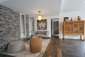 A modern living room with a grey sofa, a round ottoman, a large abstract painting, and a wooden cabinet with intricate patterns. - Villa du Château - vue imprenable sur le château médiéval (Talmont-Saint-Hilaire)