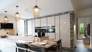 A modern kitchen with a central island, pendant lights, a flat-screen TV, and a dining area with chairs. - Villa du Château - vue imprenable sur le château médiéval (Talmont-Saint-Hilaire)