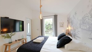 A bedroom with a bed, a TV, a wooden bench, a window, and a mural. - Villa du Château - vue imprenable sur le château médiéval (Talmont-Saint-Hilaire)
