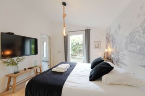 A bedroom with a bed, a TV, a wooden bench, a window, and a mural. - Villa du Château - vue imprenable sur le château médiéval (Talmont-Saint-Hilaire)