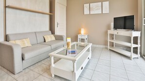 Una sala de estar con sofá, mesa de centro, mueble para TV y lámpara.