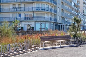 A multi-story building with balconies, a bench, and a fence with vegetation. - Cocon Kennedy - sur la baie (Les Sables d'Olonne)