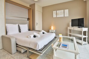 Ein Hotelzimmer mit Bett, Nachttisch, Fernseher und einem Glastisch.