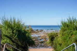 A pathway leading to a beach with rocky terrain and ocean views. - Cocon Kennedy - sur la baie (Les Sables d'Olonne)