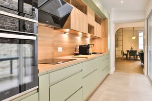 Eine moderne Küche mit Einbauofen, Kaffeemaschine und hellgrünen Schränken.