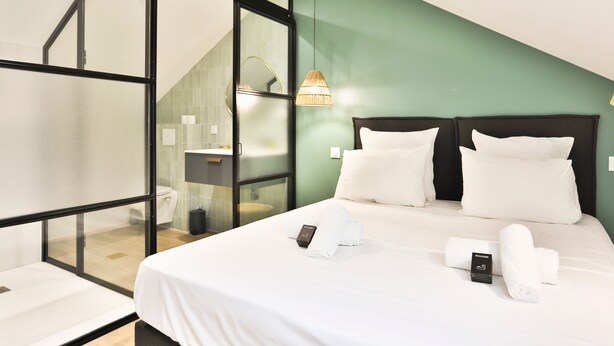 A modern hotel room with a glass partition, a bed with white linens, a bedside table, and a hanging light fixture. - Villa Babil - Four Bedroom House, Sleeps 8 (Les Sables d'Olonne)